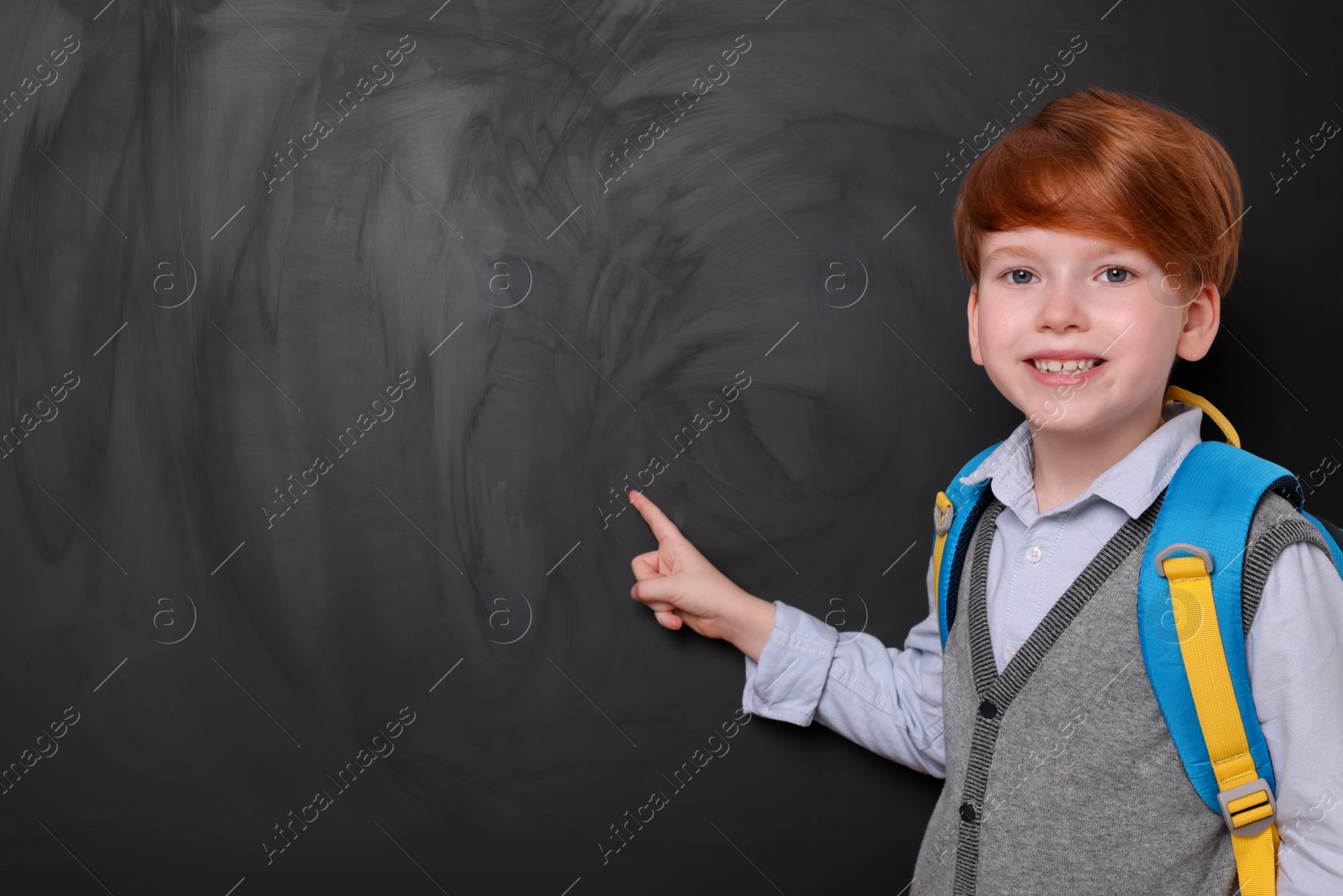 Photo of Smiling schoolboy pointing at something on blackboard. Space for text