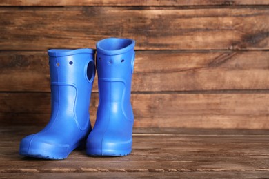 Photo of Bright blue rubber boots on wooden surface, space for text