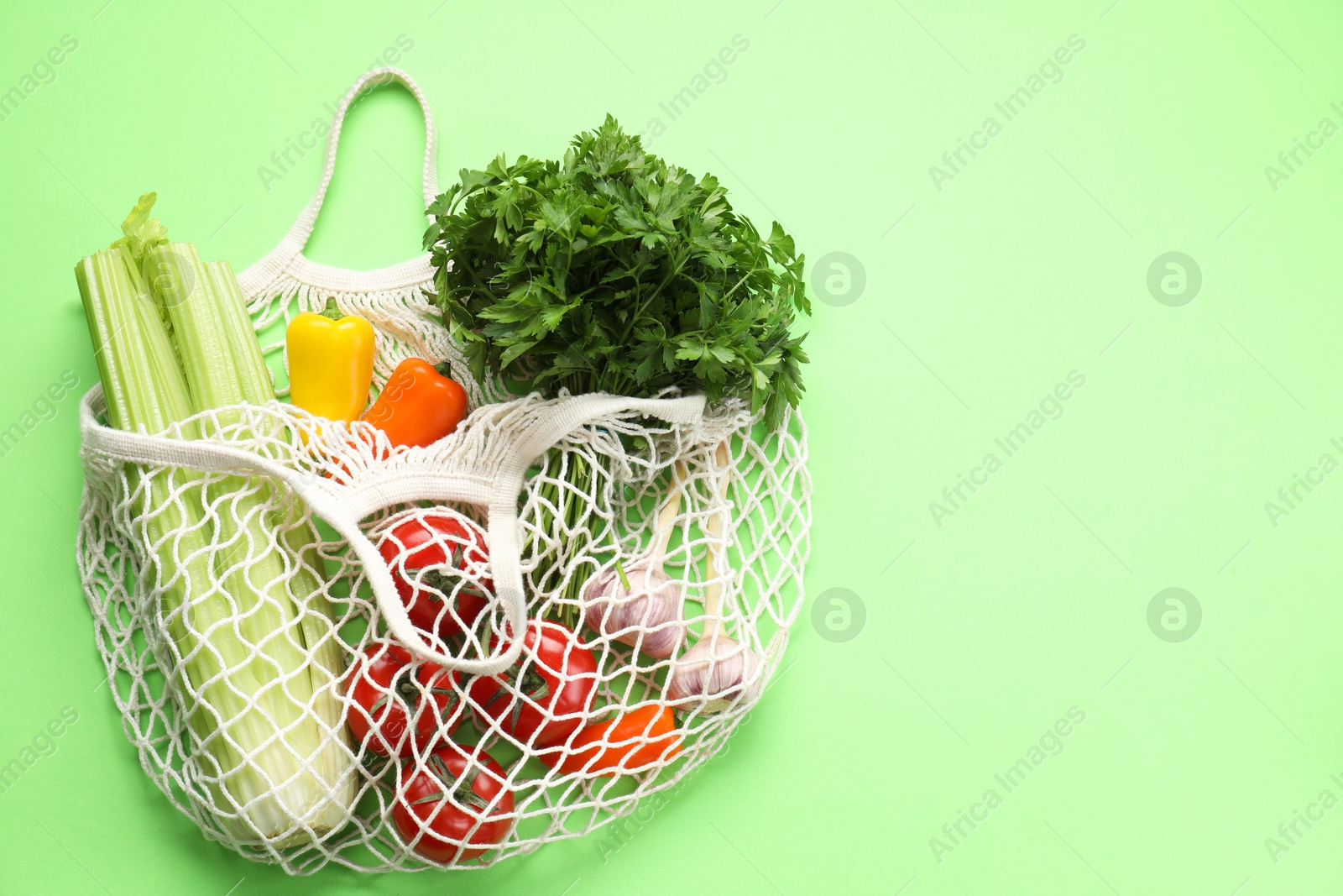 Photo of String bag with different vegetables on light green background, top view. Space for text