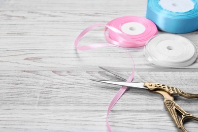 Photo of Scissors and pink ribbon on white wooden table, space for text