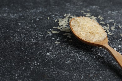Photo of Spoon with raw rice on black textured table. Space for text