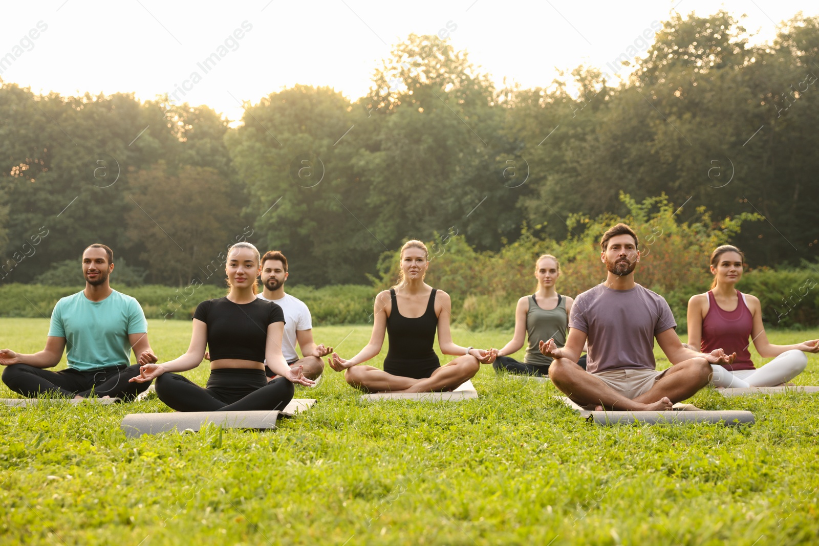 Photo of Group of people practicing yoga on mats outdoors. Lotus pose