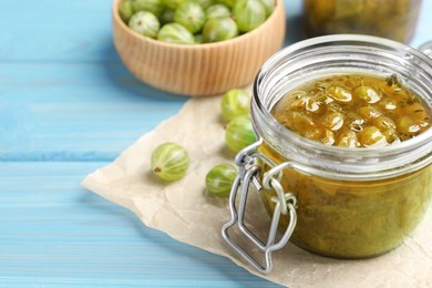 Photo of Jar of delicious gooseberry jam and fresh berries on blue wooden table, closeup. Space for text