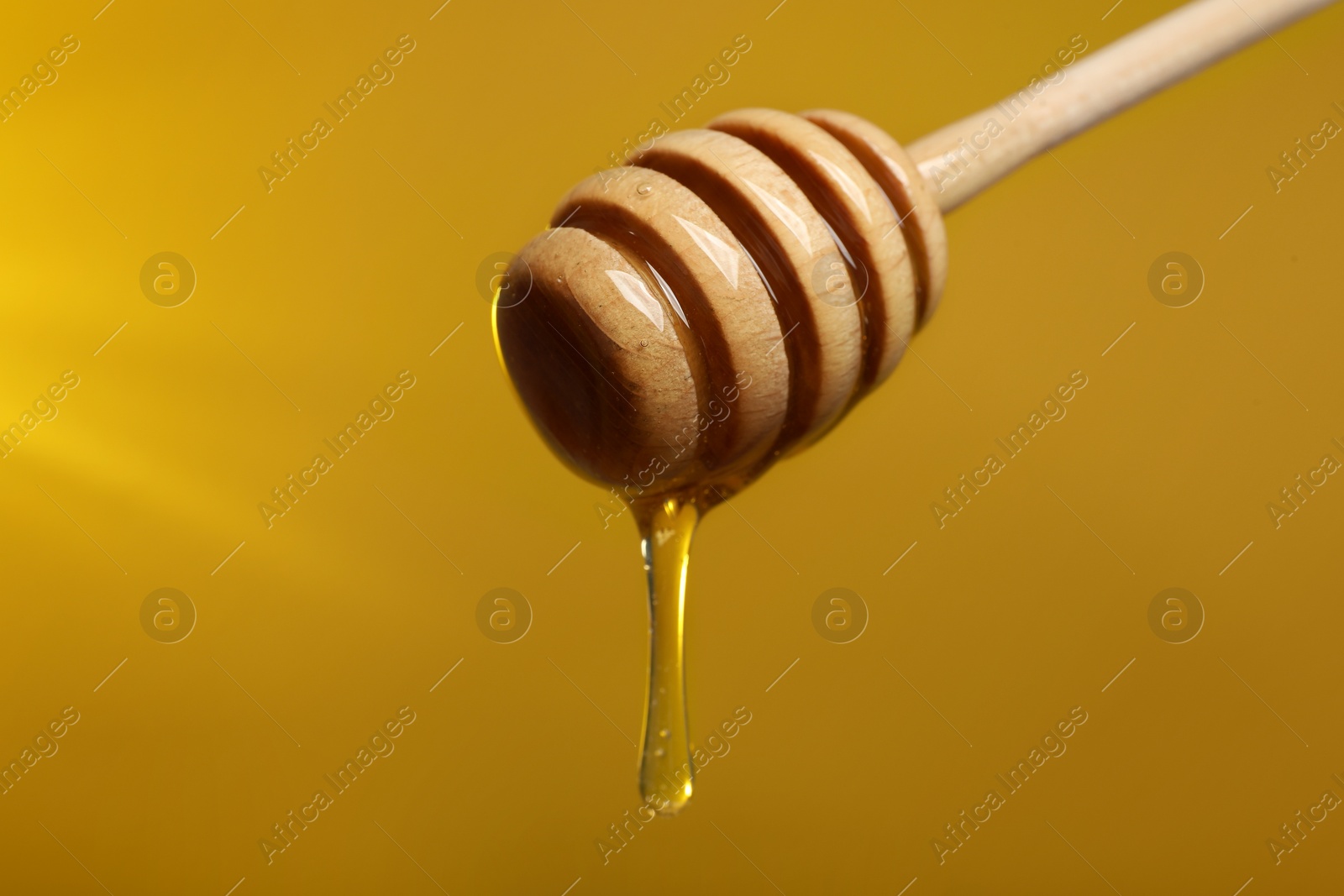 Photo of Pouring honey from dipper against golden background, closeup. Space for text