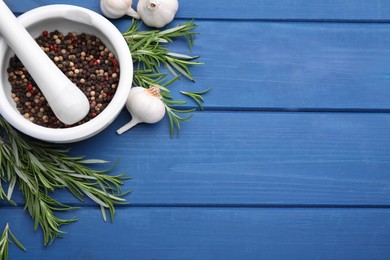 Photo of Sprigs of rosemary, mortar and garlic on blue wooden table, flat lay. Space for text