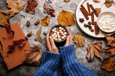 Woman with cup of hot drink at grey table, top view. Cozy autumn atmosphere