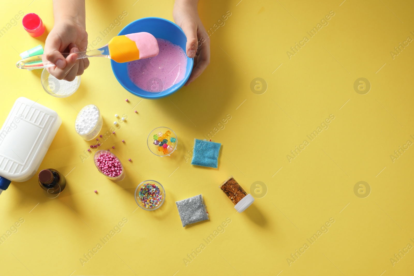 Photo of Little girl making slime toy on yellow background, top view. Space for text