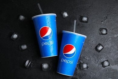 Photo of MYKOLAIV, UKRAINE - JUNE 9, 2021: Paper Pepsi cups   with water drops and ice cubes on black table, flat lay
