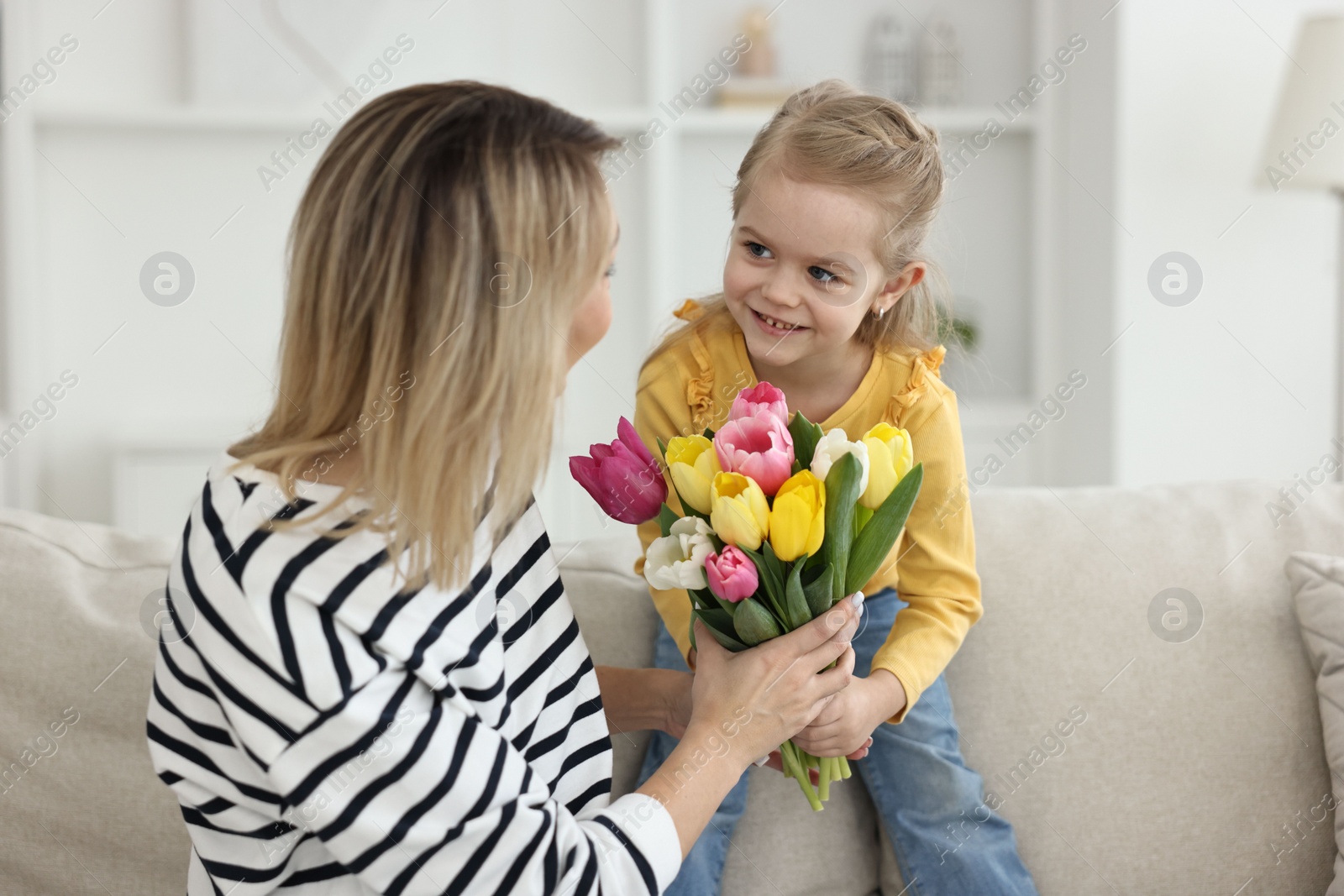 Photo of Little daughter congratulating her mom with bouquet of beautiful tulips at home. Happy Mother's Day