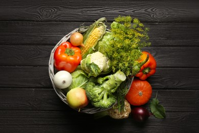 Different fresh vegetables in wicker basket on black wooden table, top view. Farmer harvesting