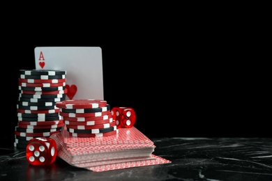 Photo of Gaming chips, dices and cards on dark marble table against black background
