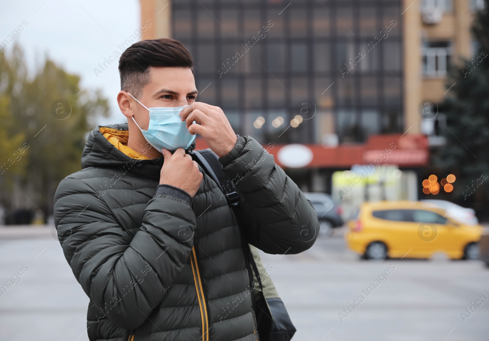 Photo of Man putting on medical face mask while walking outdoors. Personal protection during COVID-19 pandemic