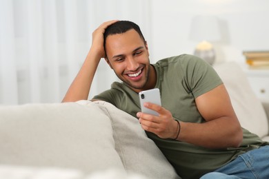 Photo of Smiling African American man with smartphone on sofa at home