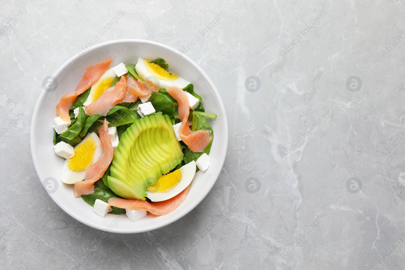 Photo of Delicious salad with boiled egg, salmon and avocado on light grey marble table, top view. Space for text