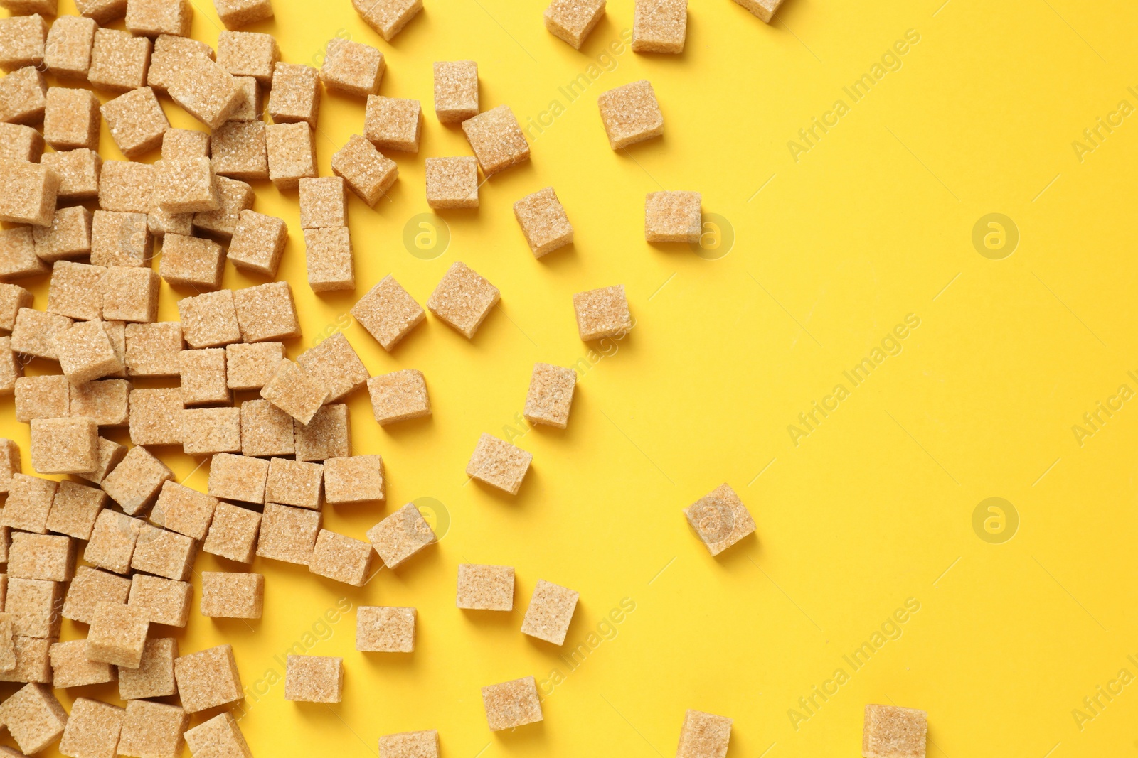 Photo of Brown sugar cubes on yellow background, flat lay. Space for text