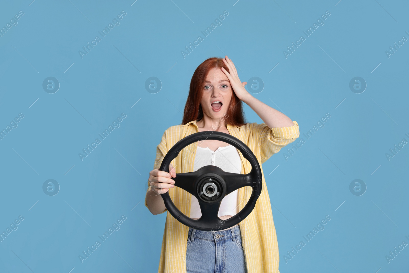 Photo of Emotional young woman with steering wheel on light blue background