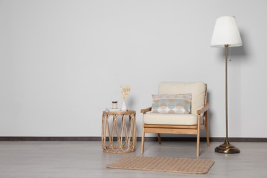 Photo of Stylish armchair, floor lamp and table near white wall, space for text. Interior design