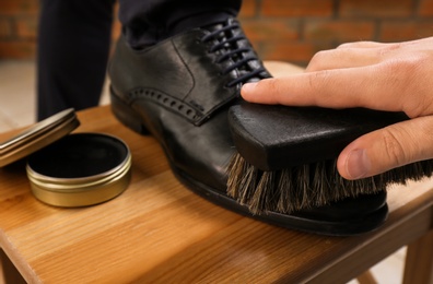 Photo of Man shining client's shoe on wooden stool indoors, closeup