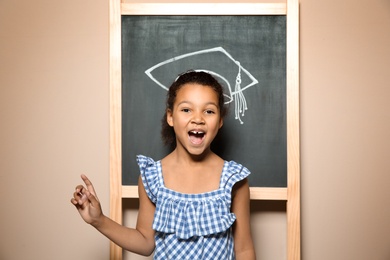 Photo of African-American child standing at blackboard with chalk drawn academic cap. Education concept