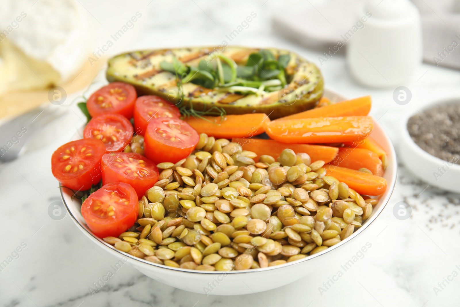 Photo of Delicious lentil bowl with avocado, tomatoes and carrots on white marble table