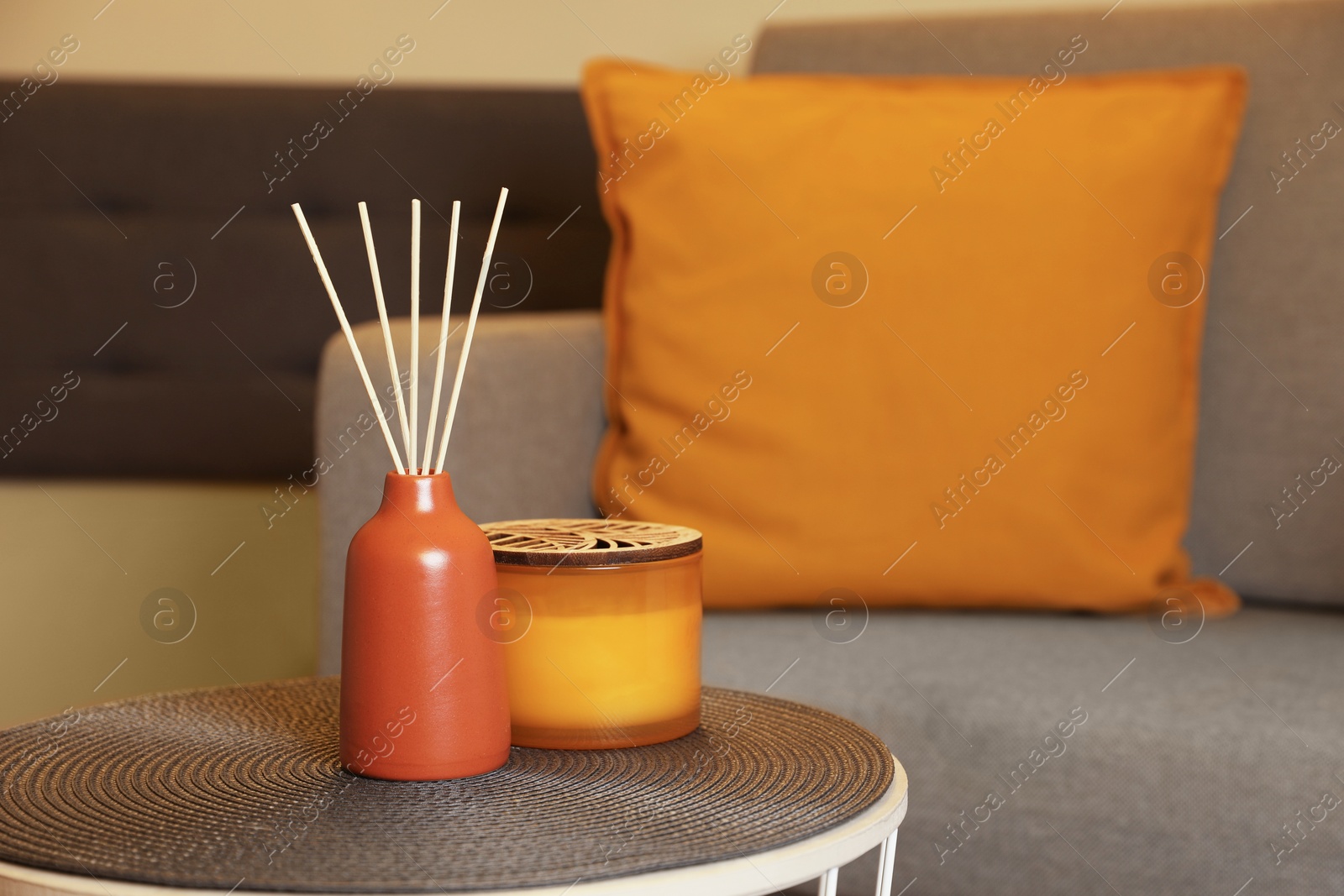 Photo of Aromatic reed air freshener and scented candle on table indoors, space for text