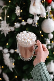 Photo of Woman with cup of delicious hot drink near Christmas tree, closeup