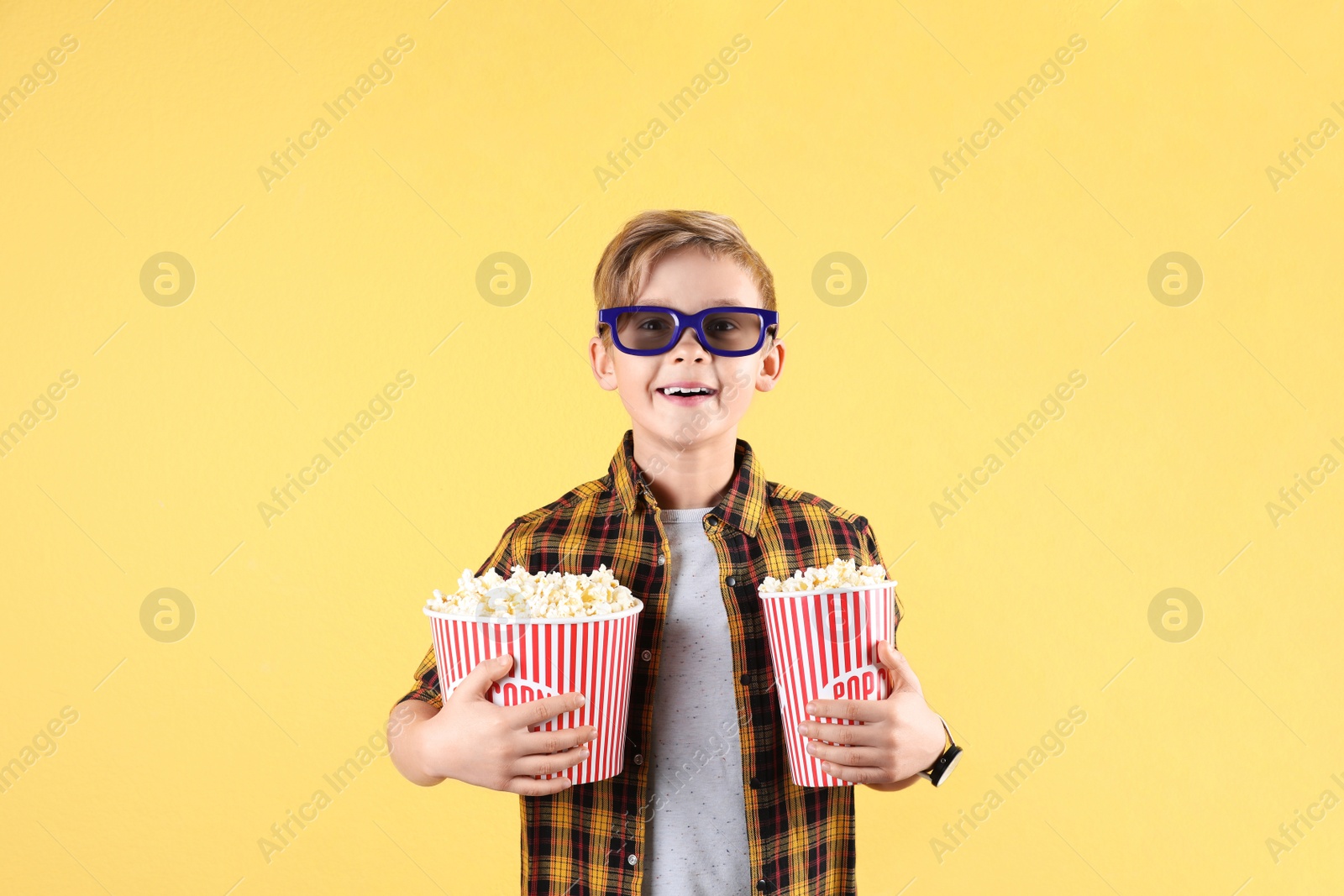 Photo of Cute boy in 3D glasses with popcorn buckets on color background