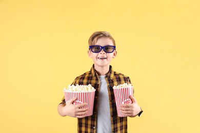 Cute boy in 3D glasses with popcorn buckets on color background