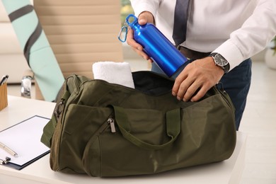 Businessman packing sports stuff for training into bag in office, closeup