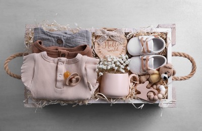 Photo of Wooden box with baby clothes, booties and toys on grey background, top view
