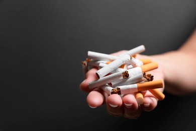 Photo of Stop smoking. Woman holding broken cigarettes on black background, closeup. Space for text