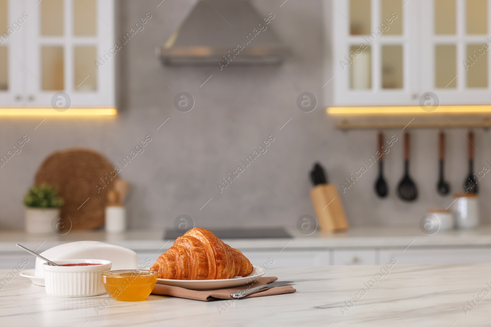 Photo of Breakfast served in kitchen. Fresh croissant, jam and honey on white table. Space for text