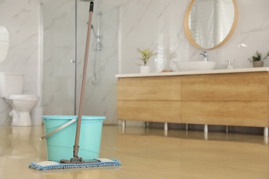 Photo of Bucket and mop on floor at home, space for text. Cleaning equipment