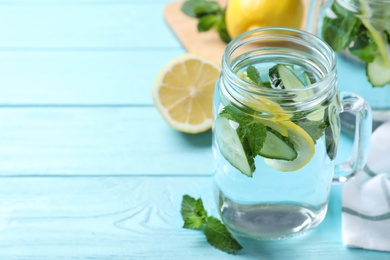 Photo of Refreshing water with cucumber, lemon and mint on light blue wooden table, closeup. Space for text