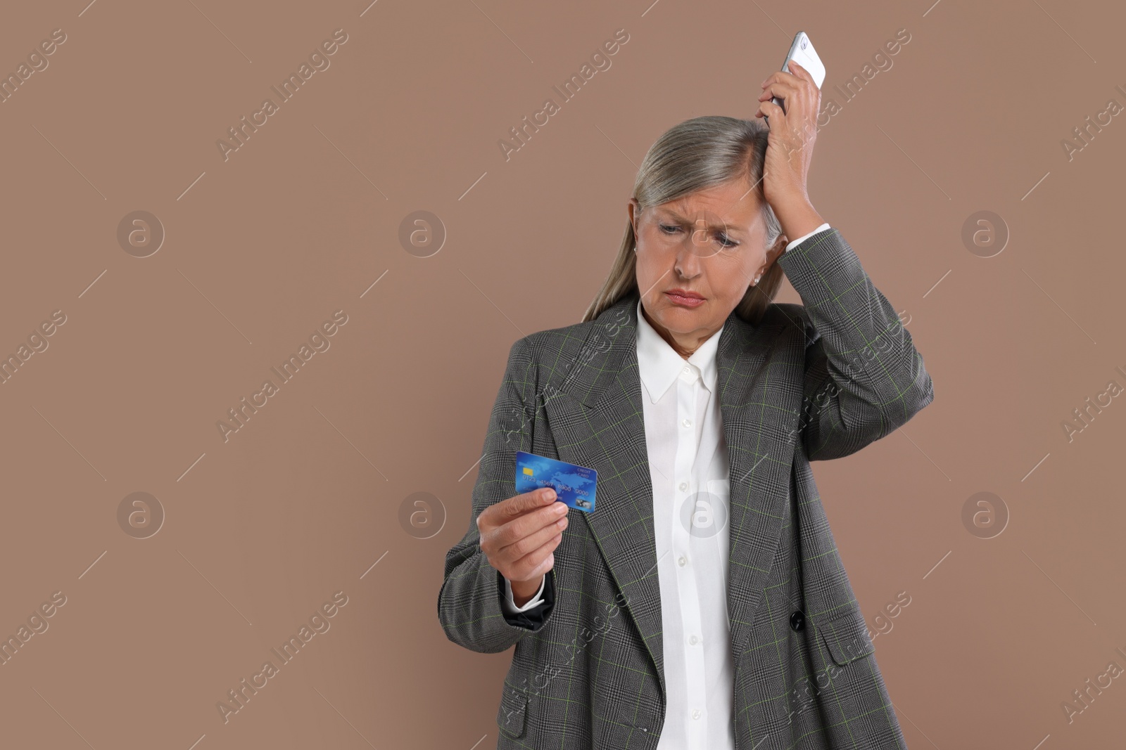 Photo of Upset businesswoman with credit card and smartphone became fraud victim on brown background, space for text