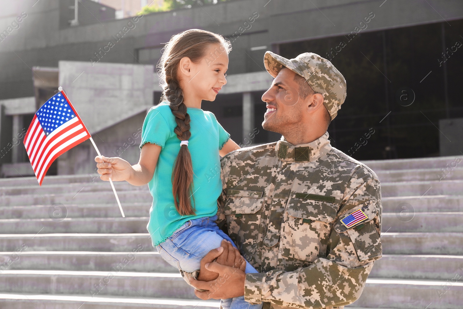 Photo of Soldier and his little daughter with American flag outdoors. Veterans Day in USA