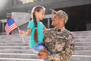 Soldier and his little daughter with American flag outdoors. Veterans Day in USA