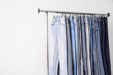Photo of Rack with different jeans on light background. Space for text