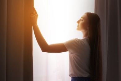 Photo of Happy woman opening stylish curtains at home