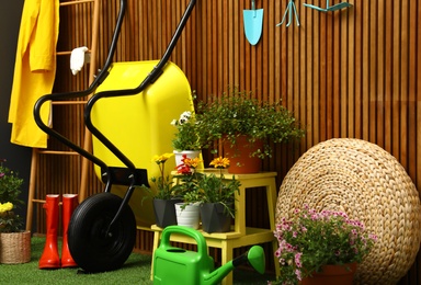 Photo of Gardening tools with wheelbarrow and flowers near wooden wall