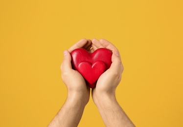Photo of Man holding decorative hearts in hands on color background, closeup