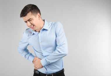 Young man suffering from flank pain on light background