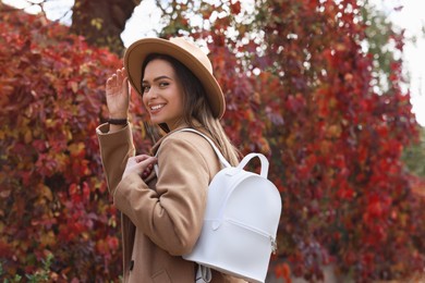 Photo of Beautiful young woman with stylish white backpack in autumn park