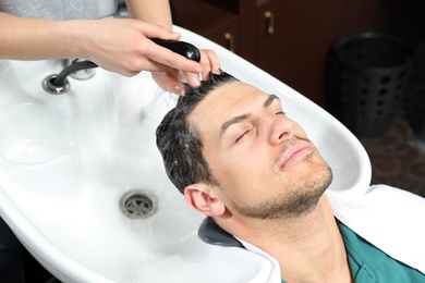 Photo of Stylist washing client's hair at sink in beauty salon