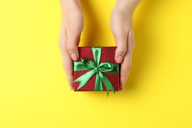 Christmas present. Woman holding beautifully wrapped gift box on yellow background, top view