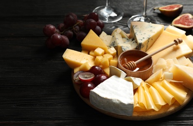 Different types of delicious cheese served on black wooden table, closeup. Space for text