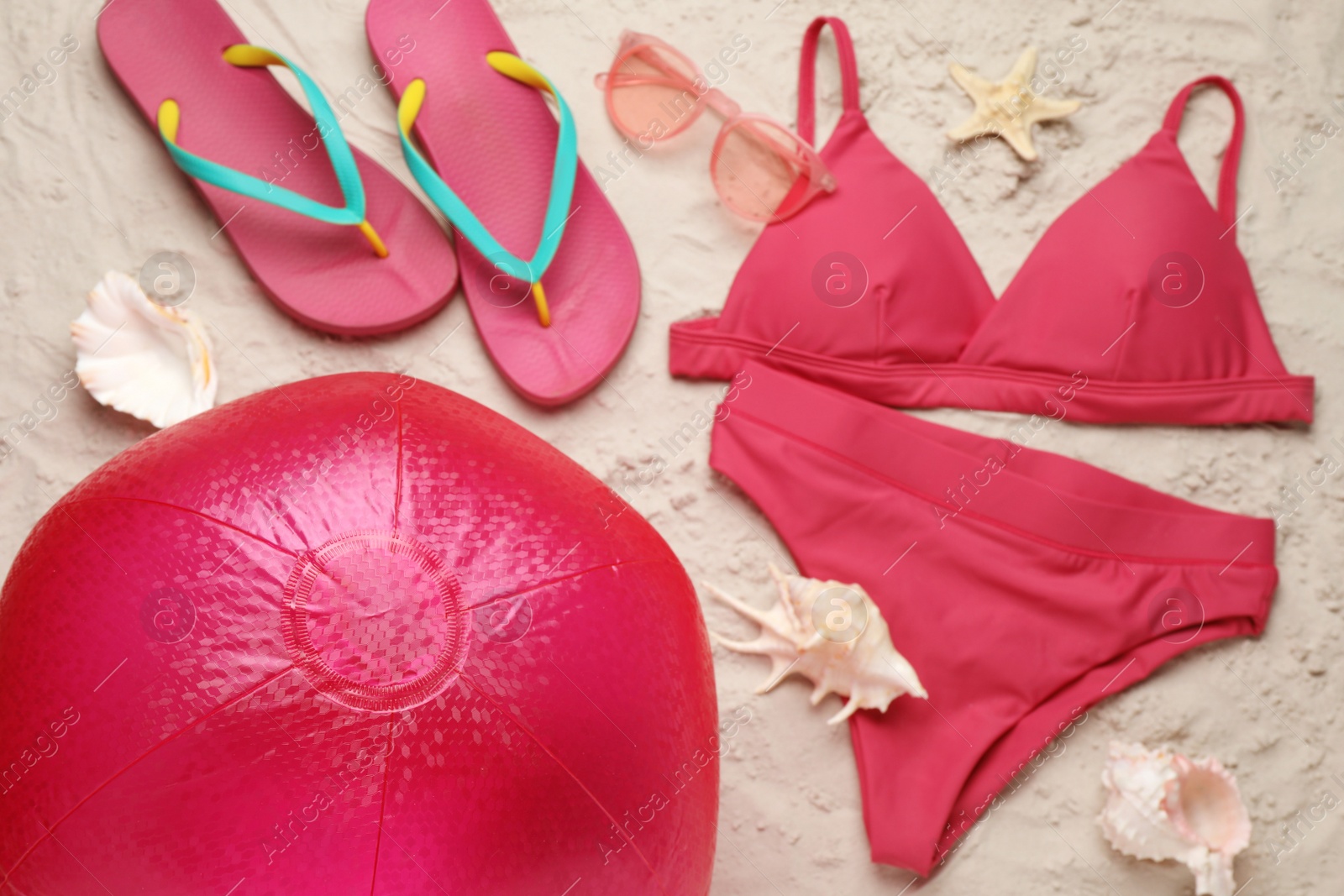 Photo of Bright beach ball and other accessories on sand, flat lay