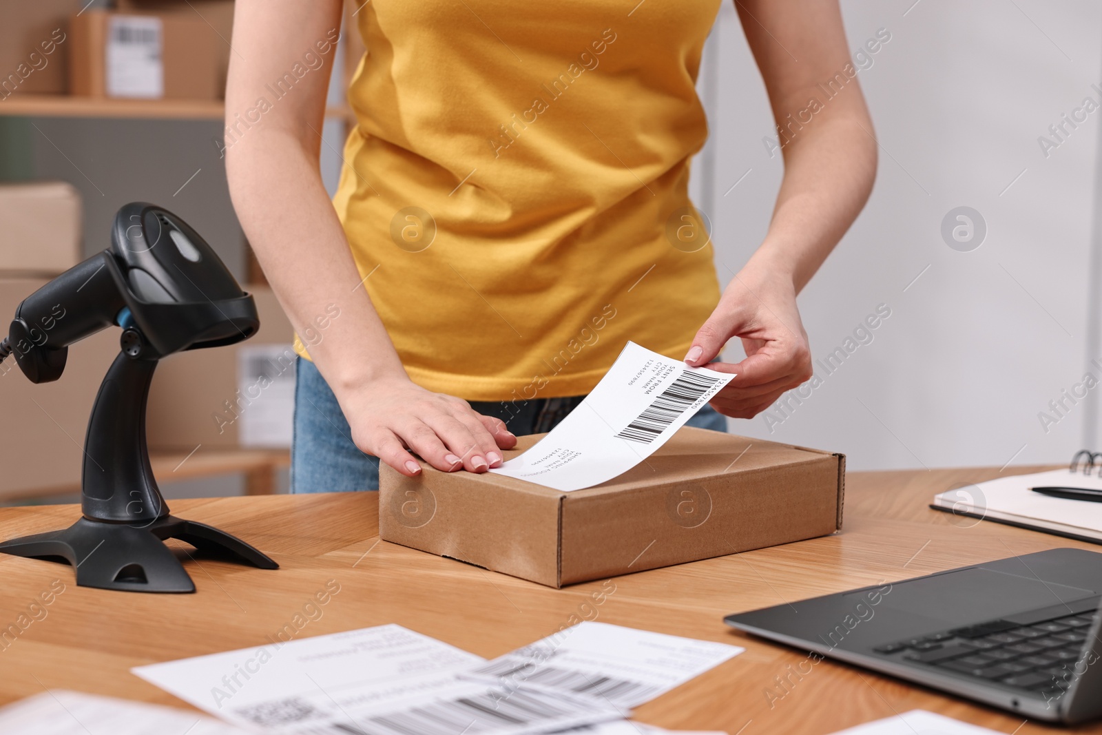 Photo of Parcel packing. Post office worker sticking barcode on box at wooden table indoors, closeup