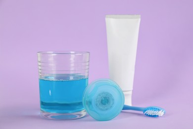 Photo of Mouthwash, toothbrush, paste and dental floss on violet background