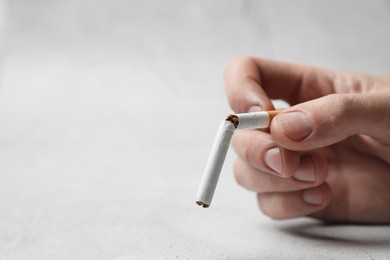 Stop smoking. Man holding broken cigarette on light background, closeup. Space for text